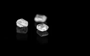 Cloro Amor-Sodio - Fotografía macro en blanco y negro de tres cristales de sal sobre una superficie negra altamente reflectante.